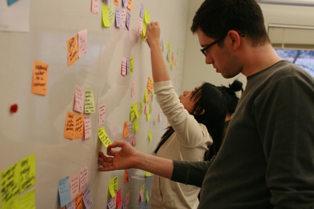James, standing at large whiteboard looking at a sticky note